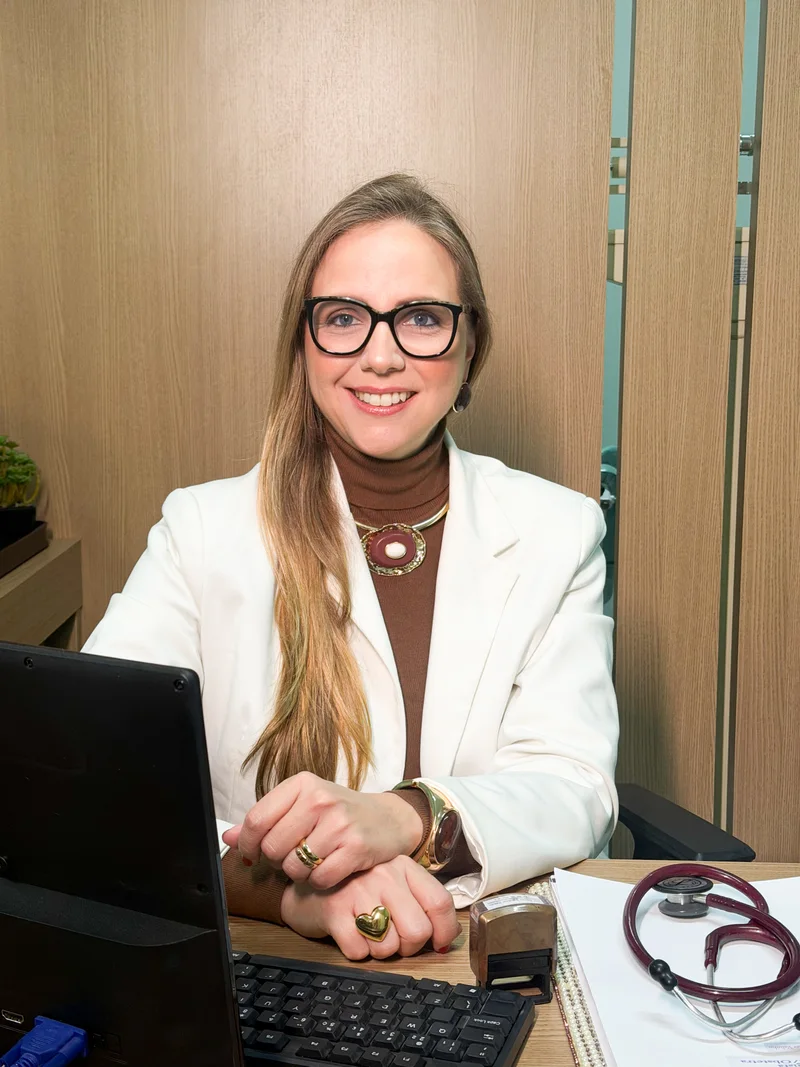 Dra. Sumara Valinho sorrindo, sentada à mesa do consultório